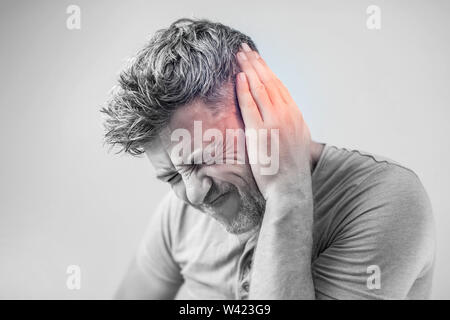 Di sesso maschile di dolore alle orecchie di toccare la sua dolorosa testa isolata su sfondo grigio Foto Stock