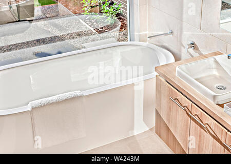 Vasca da bagno moderno con area di lavaggio in un lussuoso bagno con finestra di vetro vicino al lavandino Foto Stock