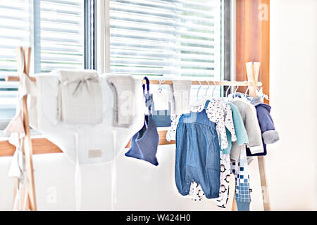 Panni per neonati o bambini vestiti appesi al tubo di legno appendiabiti accanto alla finestra di flussi che la luce del sole, ci sono i modelli e design su abiti Foto Stock