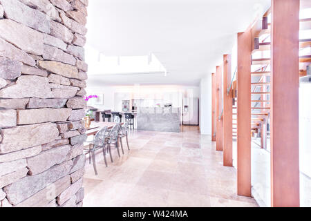 Casa di lusso all'interno con pareti in pietra e soffitti a travi in legno Scale sulle piastrelle del pavimento accanto alla zona pranzo in cucina sotto il soffitto bianco Foto Stock