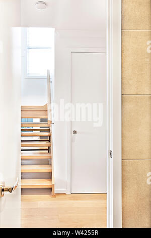 Interno di una casa della porta d'ingresso con una porta aperta al corridoio in legno attraverso le scale con passi al di sopra, la porta chiusa in bianco accanto al wa Foto Stock