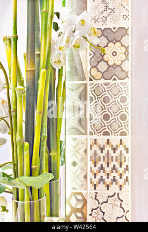 Verde di canne di bambù come un elemento decorativo in un bicchiere a fianco di una parete con motivi di bianco fiori è venuto attraverso la pianta con foglie verdi in Foto Stock