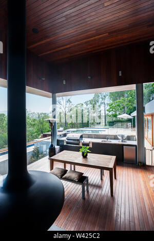 Elevato angolo di visione di un patio moderno realizzato nel pavimento in legno e il soffitto comprendente un gas grill accanto a un banco, ci sono finestre di vetro che mostrava il outsi Foto Stock