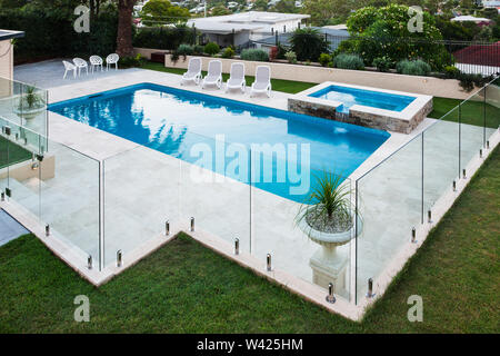 Moderna piscina coperta con pannelli di vetro accanto a un prato verde giardino inclusi alberi e sedie Foto Stock