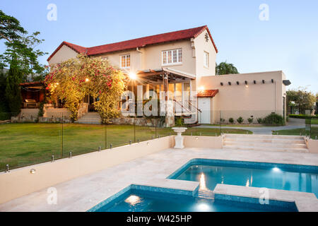 Palazzo moderno decorato con elementi naturali come il giallo gli alberi e le vigne accanto a erba verde prato e giardino e piscina dalla parte anteriore Foto Stock