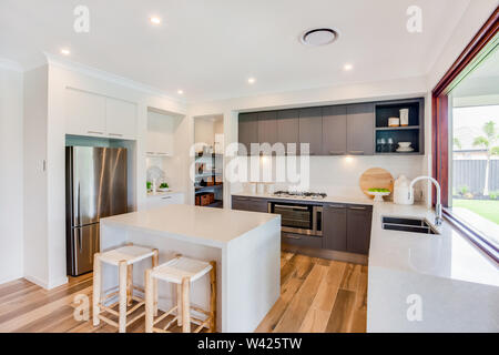 Una cucina componibile in bianco a contrasto e tonalità metallico, avente un adiacente snack counter per due persone, che si affaccia sul prato. Foto Stock