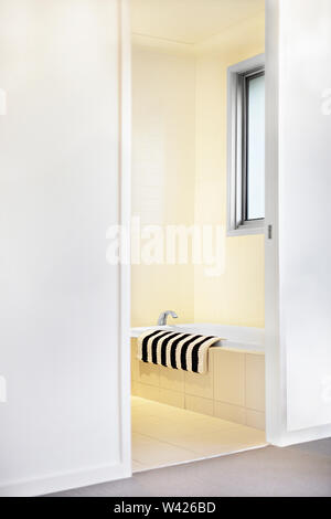Bagno ingresso e una vasca da bagno con un asciugamano in prossimità di un rubinetto di argento sulle piastrelle, vi è una finestra fissato alla parete gialla. Le porte di ingresso si apre a un mod Foto Stock