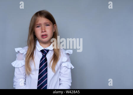 Piccolo schoolgirl ricopre la faccia, ritratto di pianto. Preteen ha sottolineato, spaventata bambino nascondere, asciugare le lacrime. Allievo, studente in uniforme scolastica. Si torna a scuola, triste, miserabile giovane ragazza pronta per la classe Foto Stock