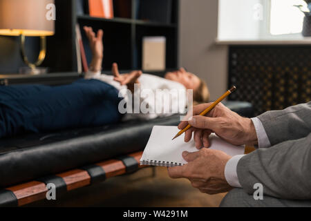 Maschio di psicoterapeuti mani rendendo note nel suo blocco note Foto Stock