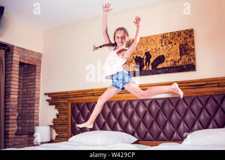 Giovane ragazza divertirsi saltando sul letto in camera da letto Foto Stock