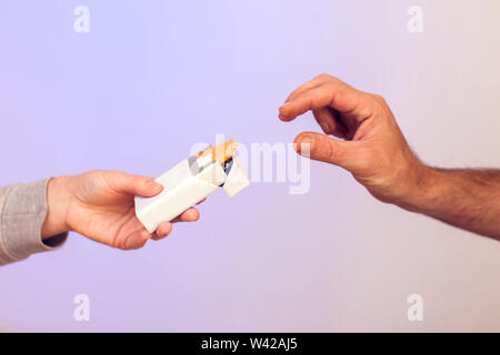 Primo piano dei maschi di mano azienda sigarette Pack e lo offrono a un altro uomo. La gente, la sanità e il concetto di fumare. Foto Stock