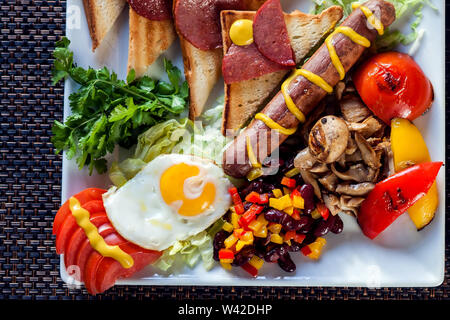 La completa prima colazione inglese inclusa salsicce, pomodori grigliati e funghi, uova, pancetta, fagioli al forno e pane. Foto Stock