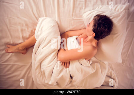 Giovane donna con capelli corti che soffrono di dolori addominali durante la seduta sul letto di casa. La gente, la sanità e il concetto di stile di vita Foto Stock