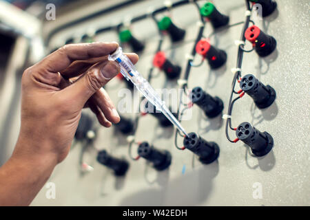 Primo piano della elettricista maschio esaminando scatola fusibili con la sonda del multimetro Foto Stock