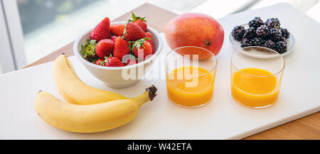 Frutta fresca e succhi di arancia isolato su bianco. Una sana prima colazione a buffet per due. Banana, fragola, blackberry e mango. Vista ravvicinata Foto Stock