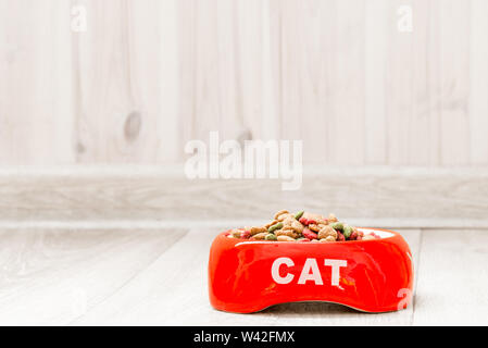 Recipiente rosso per un gatto con cibo secco sul pavimento della casa di close-up Foto Stock