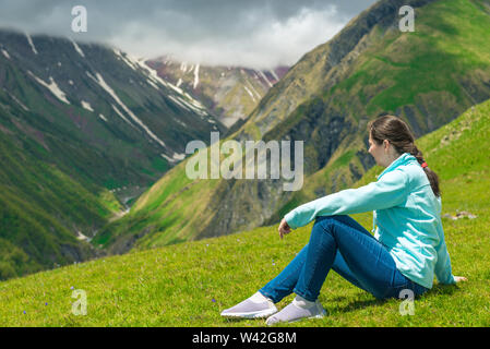 Una donna si siede sul prato e si ammira lo splendido paesaggio di montagna nella regione del Caucaso Foto Stock