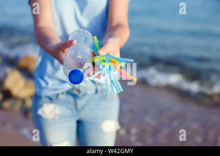 La donna mantiene la bottiglia di plastica e le cannucce in mani sulla spiaggia. Plastica concetto dell'inquinamento. Foto Stock