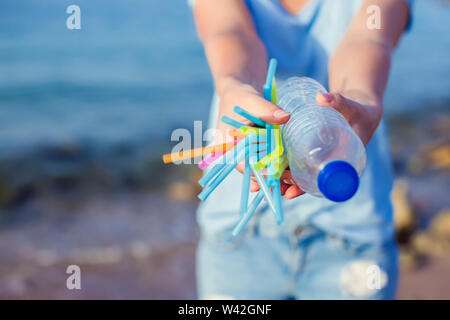 La donna mantiene la bottiglia di plastica e le cannucce in mani sulla spiaggia. Plastica concetto dell'inquinamento. Foto Stock