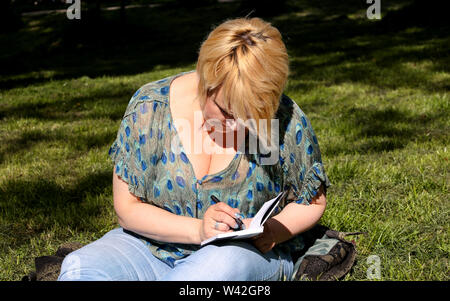 Donna e studente seduto su erba, prende appunti in notebook, apprendimento e scrive pensieri, scrive il libro che sta preparando il suo ultimo facendo i compiti. Foto Stock