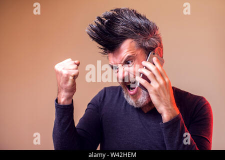 L'uomo arrabbiato con la barba e iroquis urlando al telefono. Le persone e le emozioni concetto Foto Stock