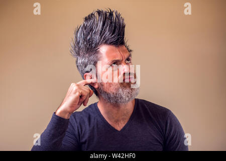 Uomo con la barba e iroquois con il dito in un orecchio. Le persone e il concetto di emozione Foto Stock