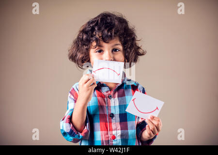 Kid boy selezionare tra positivo e negativo di espressioni. I bambini e le emozioni concetto Foto Stock