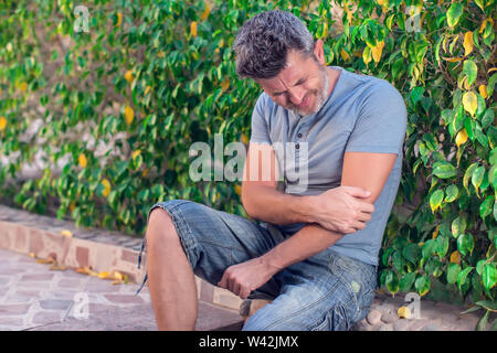 L'uomo sente forte dolore nel gomito mentre si cammina sulla strada. La gente, la sanità e la medicina concept Foto Stock