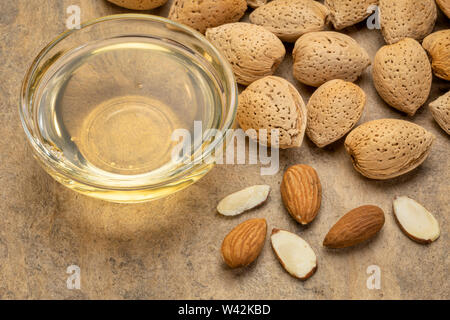 I dadi di mandorla e olio in una piccola ciotola di vetro oltre a trama della carta di corteccia Foto Stock