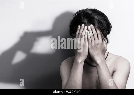 Uomo con la depressione della testa di seduta in mani con ombra di pistola che è stata rivolta la sua testa, pensando al suicidio. depressione e ansia bully vict Foto Stock