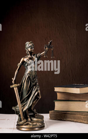 Themis figurina sorge su un bianco tavolo di legno accanto a una pila di libri antichi. Bilance legge Avvocato Concetto aziendale. - Immagine Foto Stock