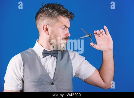 Barbiere con la barba e baffi tenere Forbici in acciaio. Toelettatura barba. Crea il tuo stile. Macho barbuto barbiere forbici per tenere i capelli tagliati. Barbiere il concetto di servizio. Imprenditore faccia rigorosa tenere forbici. Foto Stock