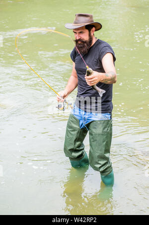 Baia di avventure di pesca. summer weekend. La pesca con la mosca. Felice barbuto fisher in acqua. fisherman Visualizza tecnica di pesca utilizzare asta. hobby e attività sportive uomo maturo di Pesca a Mosca Report di Pesca. l uomo la cattura del pesce. Foto Stock