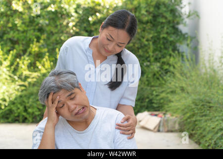 Di mezza età e uomini obesi con paralisi, piegato in bocca, mano attorcigliamento e arti debole in una sedia a rotelle stanco e senza speranze e avente una moglie t permanente Foto Stock