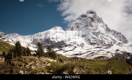 Vista del paesaggio del versante sud del Cervino, vista dal villaggio di Cervinia.prato verde nella parte anteriore e il cielo blu con nuvole bianche al di sopra di montagna Foto Stock
