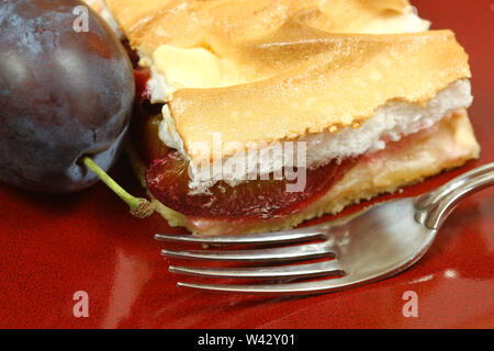 Primo piano della torta di prugne con freah prugna e la forcella sulla piastra di rosso. In autunno la torta con la meringa Foto Stock