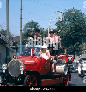 Zwei junge Frauen fahren mit einer Musikertruppe auf einem Mercedes Oldtimer in der Innenstadt Münchens in den 1980er Jahren umher. Due giovani donne andare in giro con una troupe di musica su una Mercedes auto d'epoca nel centro cittadino di Monaco di Baviera negli anni ottanta. Foto Stock