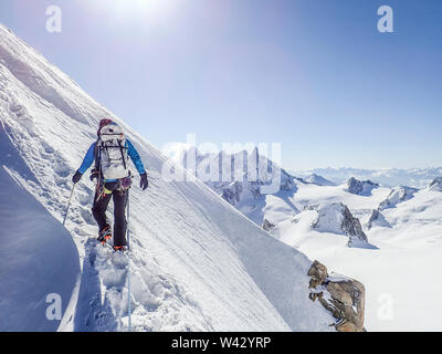 Donna alpinista ascende un ripido pendio di neve in condizioni di bluebird Foto Stock