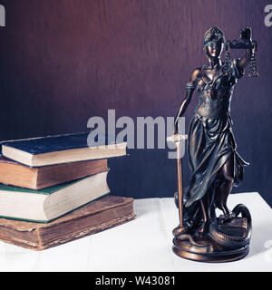 Themis figurina sorge su un bianco tavolo di legno accanto a una pila di libri antichi. Bilance legge Avvocato Concetto aziendale. - Immagine Foto Stock