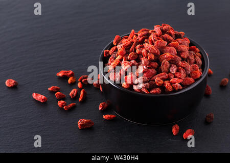 Super Brain food dry Goji berry in nero coppa in ceramica su pietra ardesia scheda con spazio di copia Foto Stock