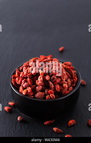 Super Brain food dry Goji berry in nero coppa in ceramica su pietra ardesia scheda con spazio di copia Foto Stock