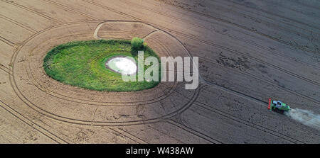Petersdorf, Germania. 18 Luglio, 2019. Una mietitrebbia da Markus Grund farm di raccolti di grano di inverno su un campo di grano in Oder-Spree distretto a una cosiddetta "oll', un piccolo foro per l'acqua circondato da prati (fotografia aerea con un drone). Tale "ölle' spesso è emersa come un risultato di età di ghiaccio nella parte nord-orientale della Germania. Come biotopi, essi formano ecologicamente preziosi isole in agriculturally usato pesantemente aree. Credito: Patrick Pleul/dpa-Zentralbild/ZB/dpa/Alamy Live News Foto Stock