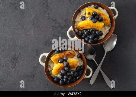 Piastra con i fiocchi d'avena, banane fritte, mirtillo, cioccolato su uno sfondo scuro vista dall'alto. Tavolo per la colazione concept Foto Stock