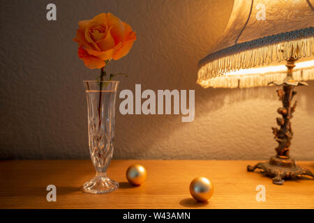 Un grande Whisky Mac Hybrid Tea Rose fiori recisi in un taglio vaso di vetro illuminato da una lampada da tavolo Foto Stock