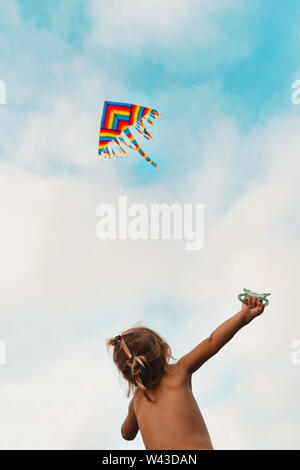 Bambino felice lancia un aquilone, baby cercando fino a un multi-colore kite volare nel cielo, infanzia felice, kid godendo le vacanze estive Foto Stock