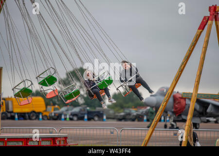 RAF Fairford, Glos, Regno Unito. Il 19 luglio 2019. Giorno 1 del Royal International Air Tattoo (RIAT) con velivoli militari provenienti da tutto il mondo per assemblaggio di più grande del mondo che airshow corre da 19-21 luglio. Giorno 1 battenti display è fortemente ridotta a causa della bassa base cloud, forte pioggia e vento. Immagine: due visitatori godere di una giostra di carnevale nonostante il meteo. Credito: Malcolm Park/Alamy Live News. Foto Stock