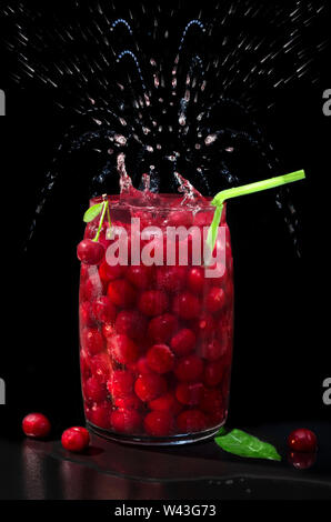 Ciliegie mature in un vaso di acqua minerale. Spray, il fuoco selettivo. Foto Stock