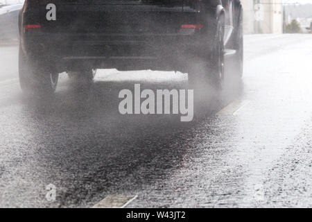 Acqua di pioggia flusso splash da ruote di auto nera si muove velocemente nella città di luce diurna con il fuoco selettivo. Piccole gocce di nebbia. Foto Stock