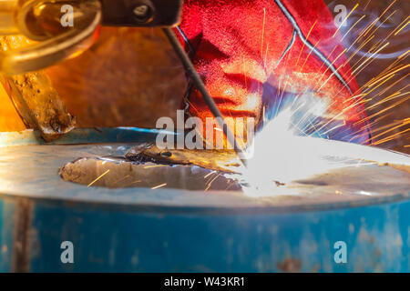 Lavoratore con Red Glove per proteggere la scintilla di luce con processo di saldatura con tubo blu metallico e luminose scintille in acciaio Foto Stock