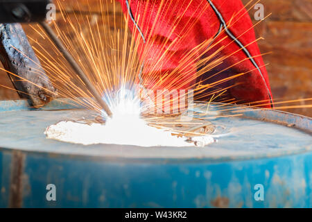 Lavoratore con Red Glove per proteggere la scintilla di luce con processo di saldatura con tubo blu metallico e luminose scintille in acciaio Foto Stock